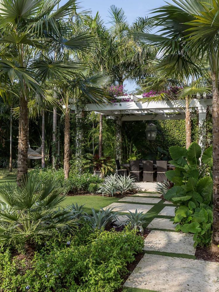 an outdoor area with palm trees, plants and stone walkway leading to a covered patio