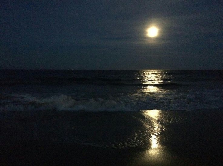 the moon is shining over the ocean on a dark night with waves coming in to shore