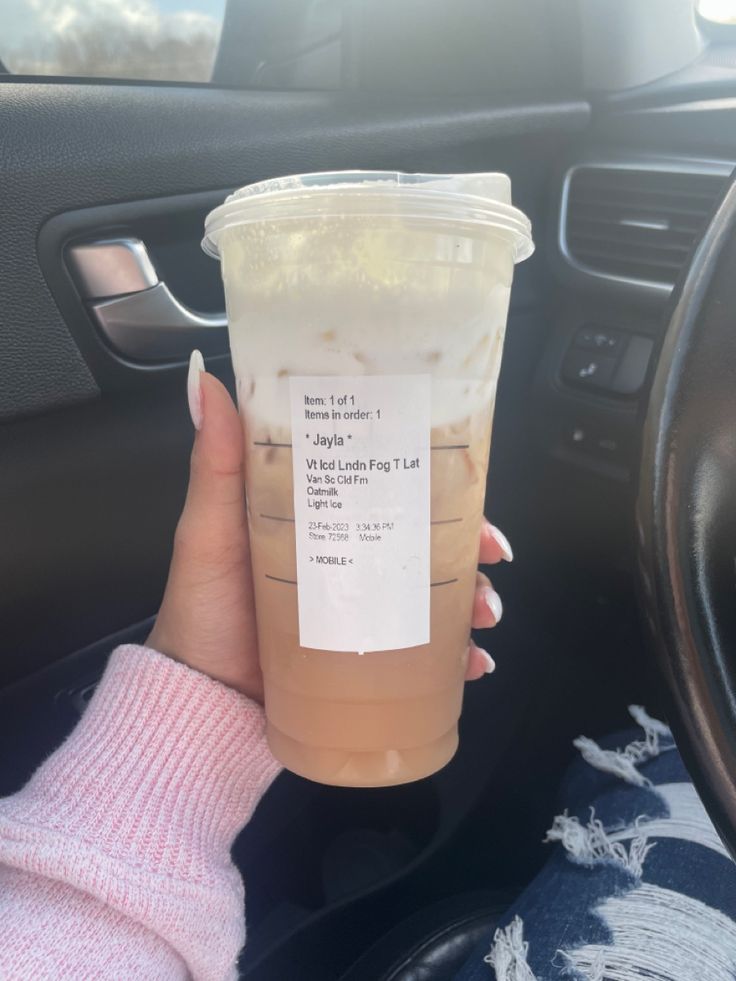 a woman holding up a cup of iced coffee in her hand while sitting in the driver's seat of a car