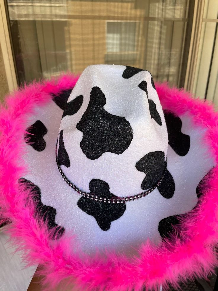 a white and black cow print hat with pink fur around the brimmings