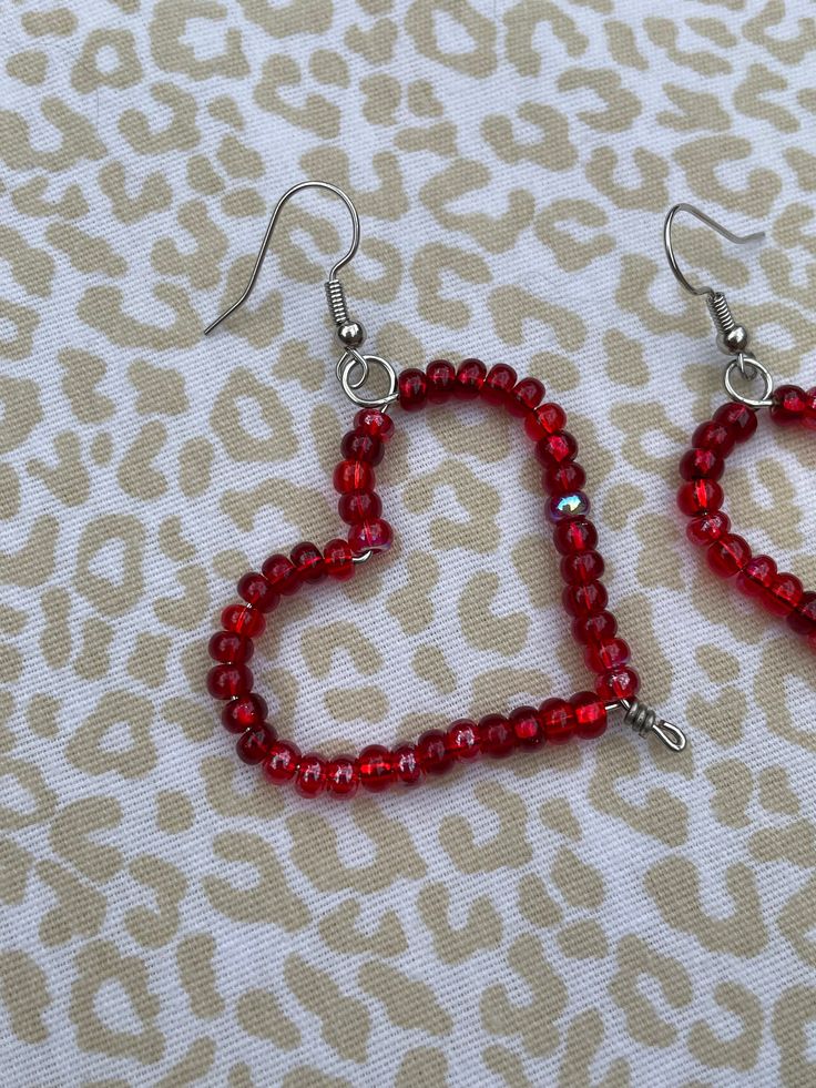 red beaded heart shaped earrings sitting on top of a leopard print tablecloth,