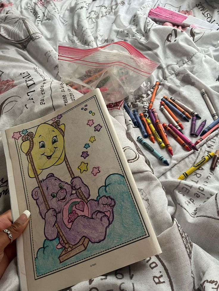 a person is holding a coloring book and some crayons on a bed with white sheets