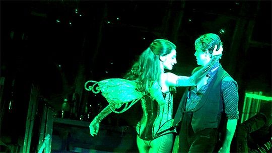 a man and woman standing next to each other in front of a green neon light