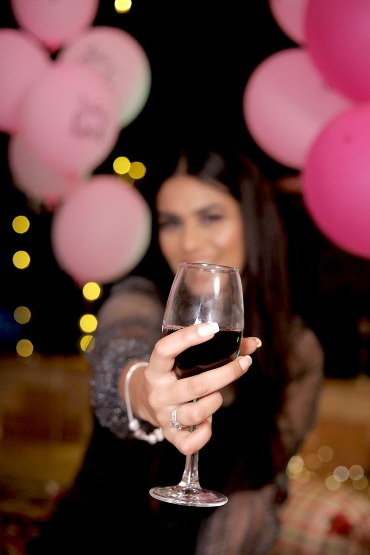 a woman holding a wine glass in front of balloons