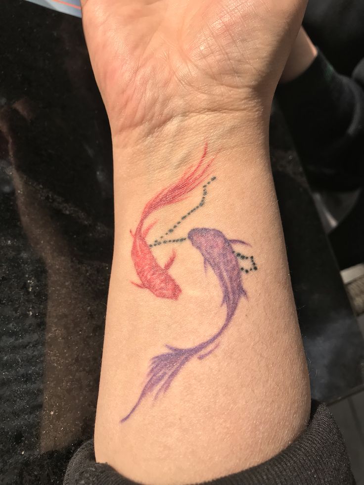 a woman's wrist tattoo with two colorful fish on the left side of her arm