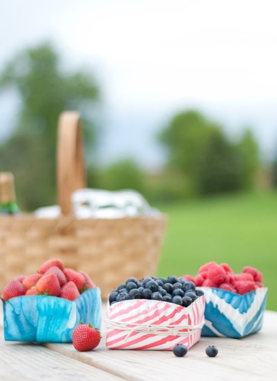 three baskets filled with berries and blueberries on top of a wooden table next to a picnic basket