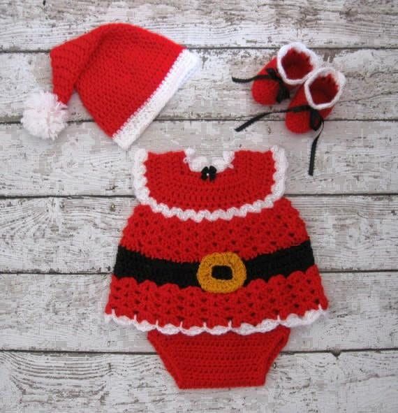 a crocheted santa suit and hat on a white wooden surface with red flowers