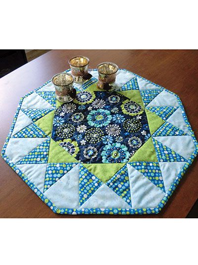 a blue and green quilted table top with two candles on it