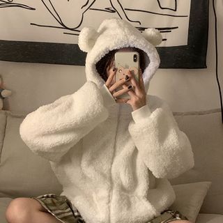 a person sitting on a couch taking a selfie with a cell phone wearing a white teddy bear robe