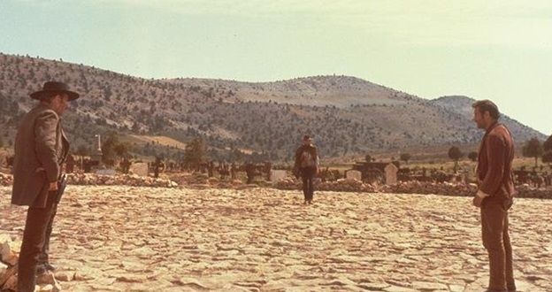 three men standing in the middle of a desert with mountains in the backgroud