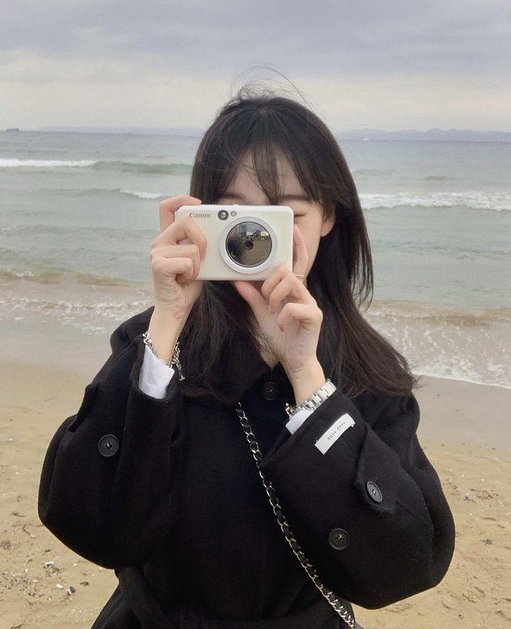 a woman taking a photo on the beach with her camera in front of her face