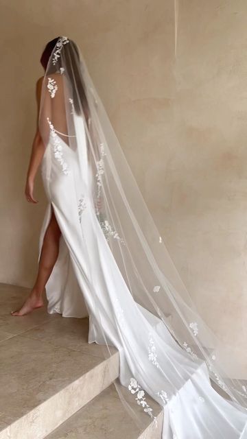 a woman in a wedding dress is walking up some stairs with her veil over her head