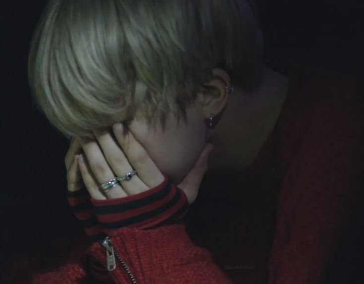 a woman with blonde hair wearing a red sweater and diamond rings on her fingers, covering her face