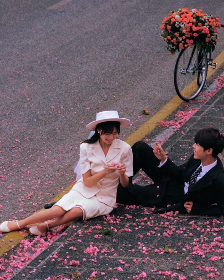 a woman sitting on the ground next to a man in a suit and white hat