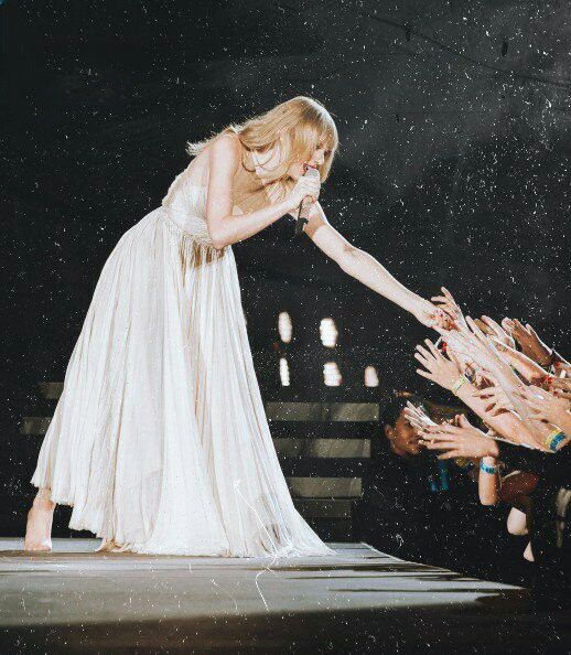 a woman in white dress standing on stage with her hands out to someone holding something