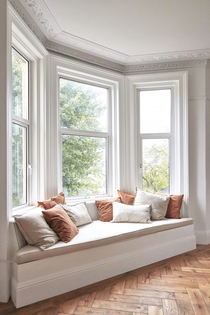 a white window seat with pillows on it in front of two windows and wood flooring