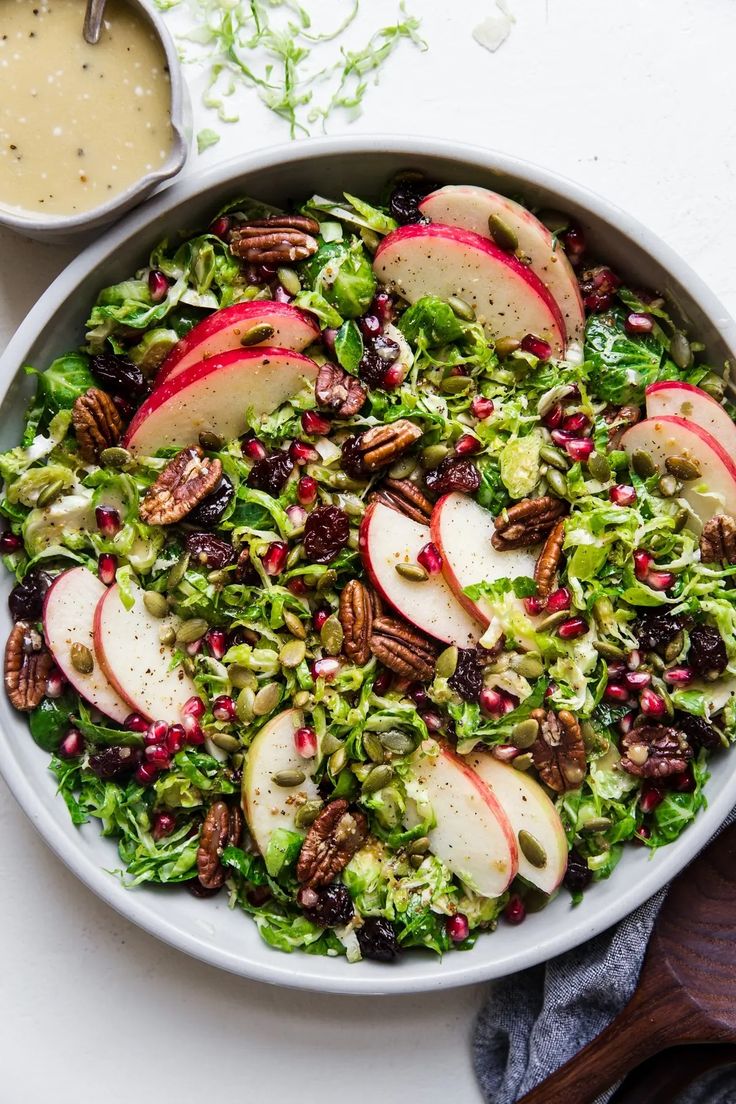 a salad with apples, cranberries and pecans in a white bowl next to a spoon