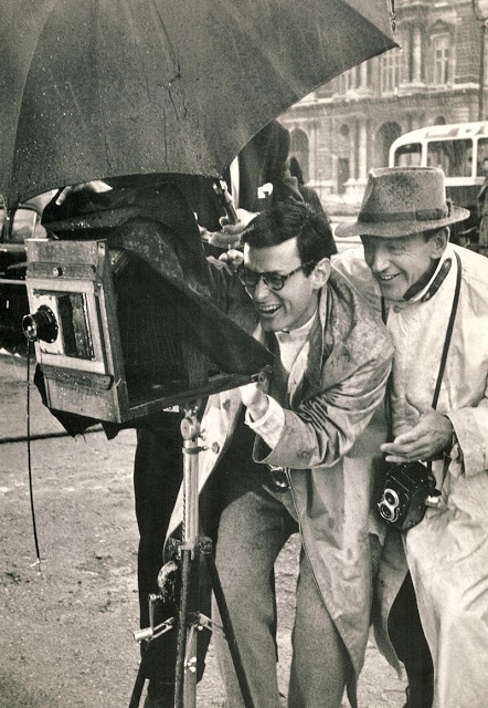 two men standing next to each other holding an umbrella over their head while another man looks at the camera