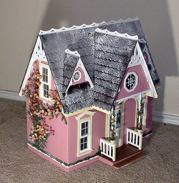 a pink doll house sitting on top of a carpeted floor next to a wall