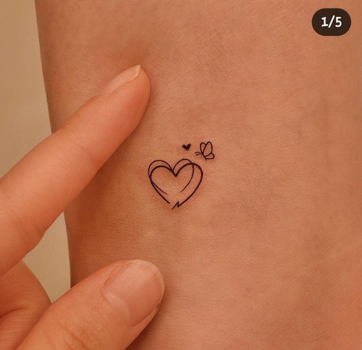 a small heart tattoo on the left side of the wrist is shown in black ink