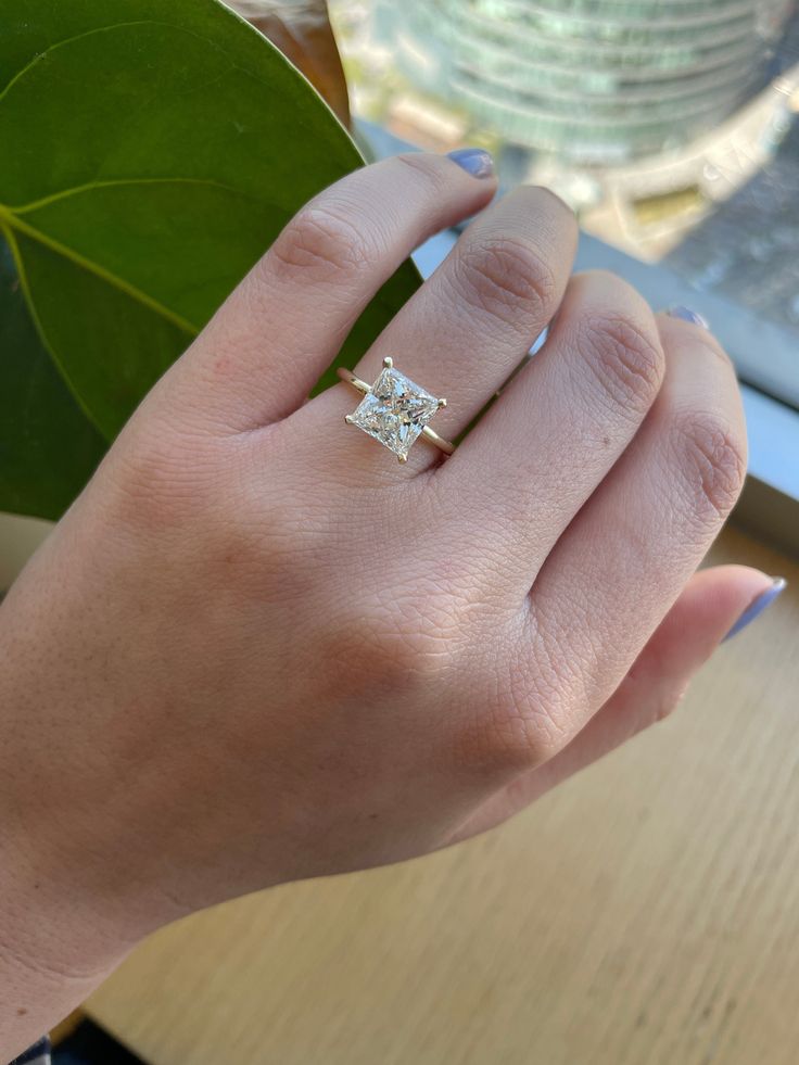 a woman's hand with a diamond ring on top of her finger, next to a green leaf