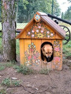 a dog in a wooden house next to a tree with flowers painted on it's side