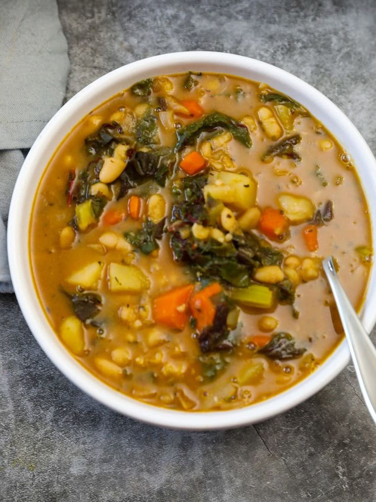 a white bowl filled with vegetable soup on top of a gray countertop next to a spoon