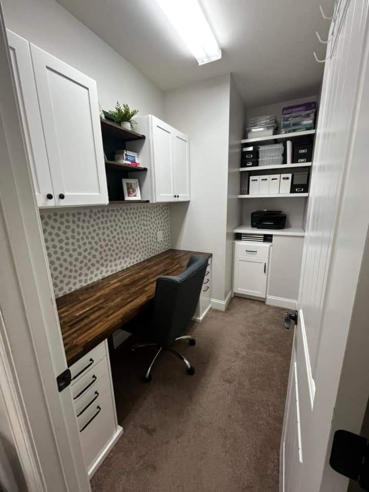 a home office with white cabinets and brown carpeted flooring is pictured in this image