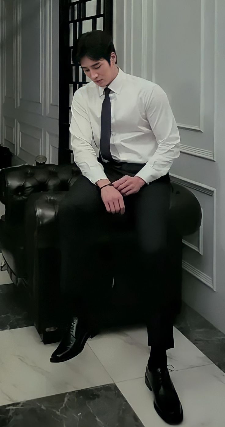 a man sitting on top of a black chair wearing a white dress shirt and tie