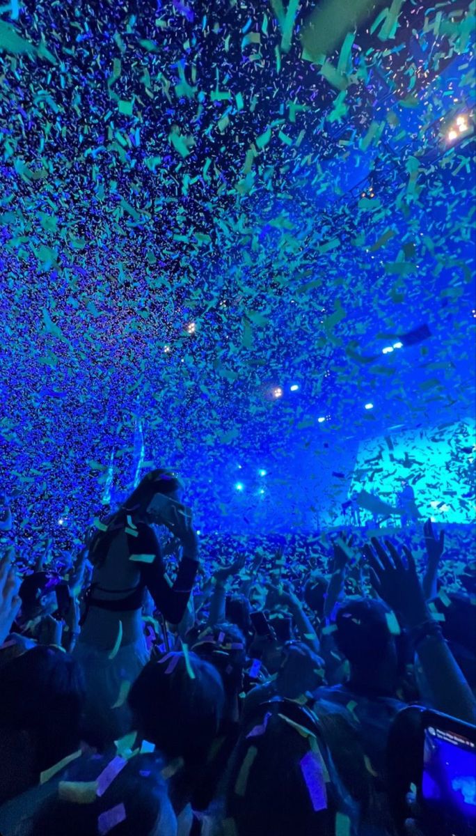 a large crowd at a concert with confetti falling from the ceiling