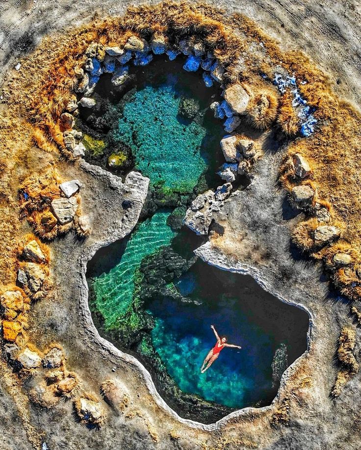 an aerial view of a man swimming in the blue pool at meadow hot springs, australia