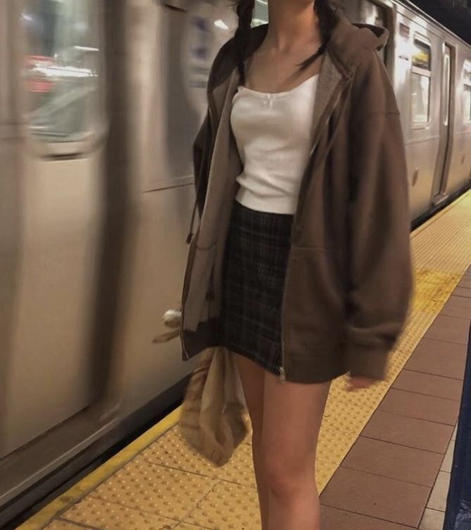 a woman standing next to a train at a subway station with her hand in her pocket