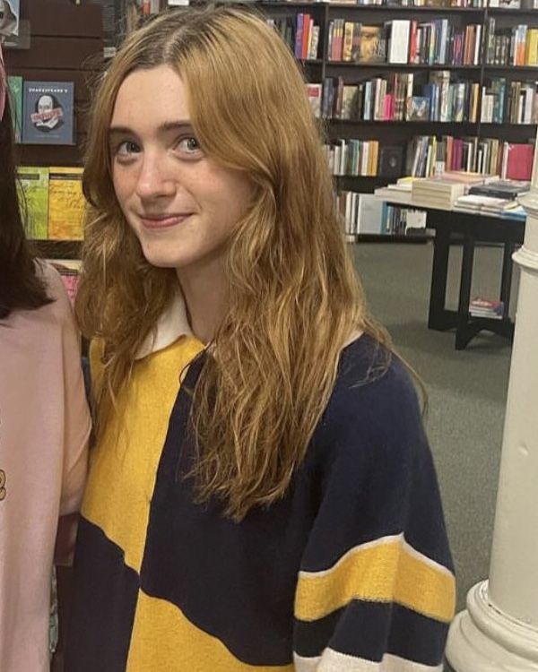 two young women standing next to each other in front of bookshelves at a library