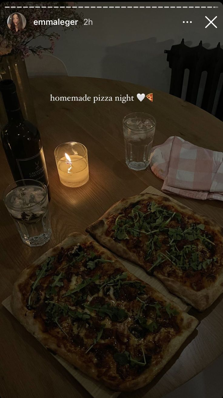 two pizzas sitting on top of a wooden table next to a candle and some glasses