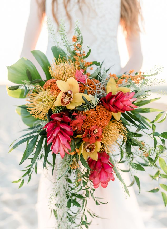 a bride holding a bouquet of flowers in her hands on the beach with sand behind her