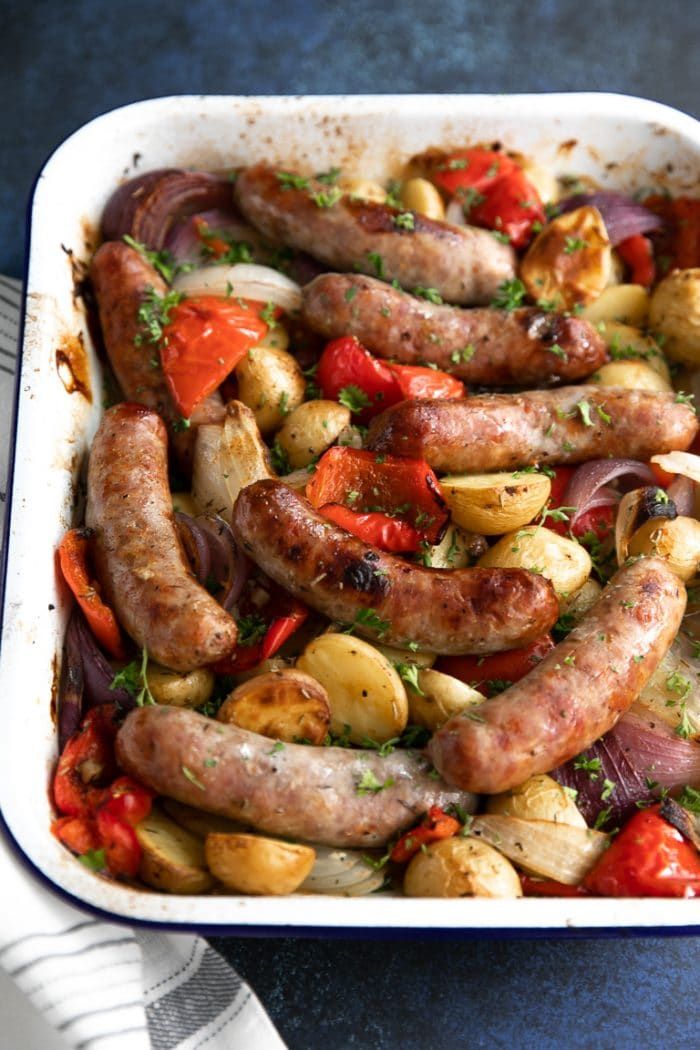 sausages and vegetables in a casserole dish on a blue tablecloth with utensils