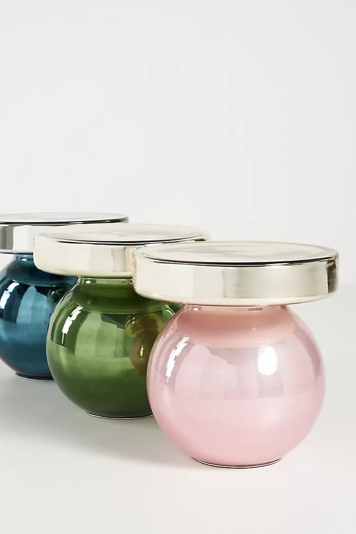 three different colored vases sitting next to each other on a white surface with silver lid