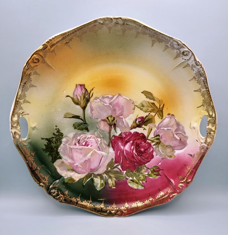 a decorative bowl with pink roses painted on the side and gold trim around the edge