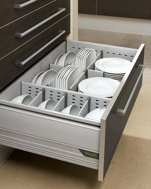 an open drawer with plates and cups in it on the floor next to a dresser