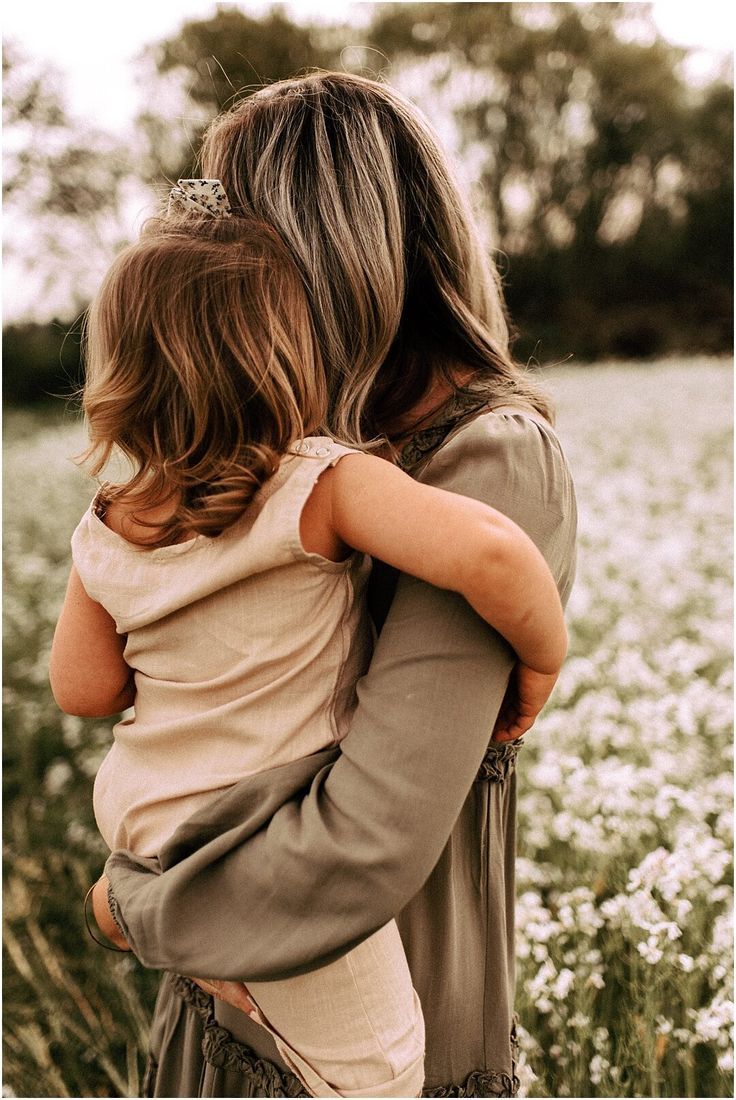 a woman holding a child in her arms while standing in a field full of flowers