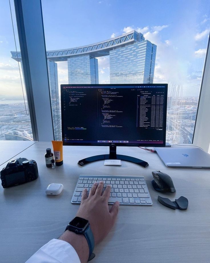 a person typing on a keyboard in front of a computer monitor with a view of the city