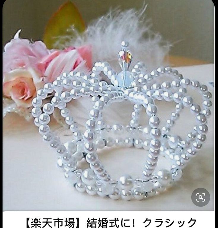 a white tiara with pearls on it and flowers in the background, sitting on a table