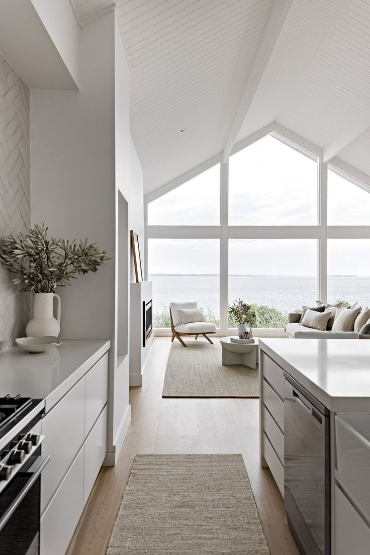 an open kitchen and living room area with large windows overlooking the ocean is shown in this image