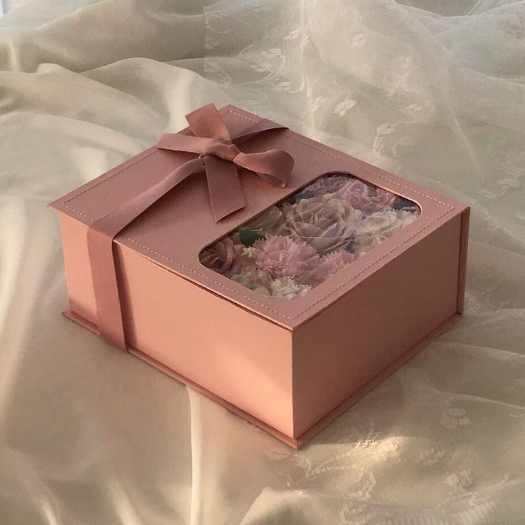 an open pink box with flowers inside on a white cloth covered bed sheeted surface