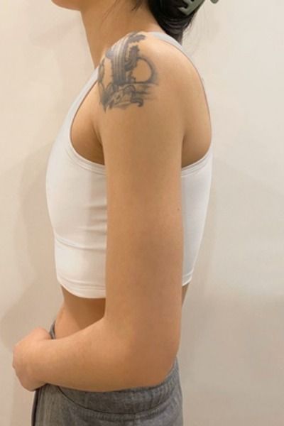 a woman with a tattoo on her arm standing in front of a wall and looking off to the side