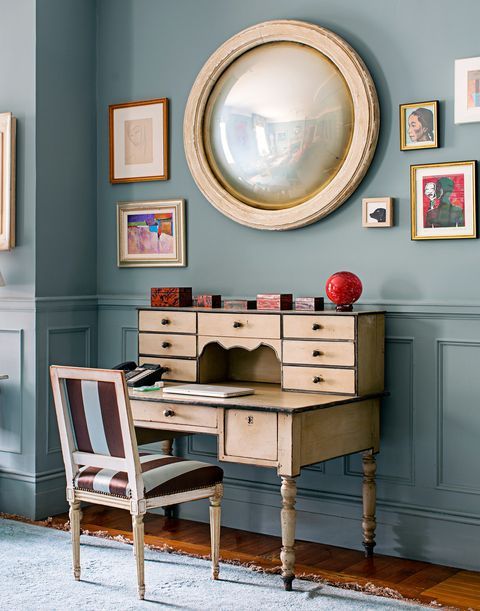 a room with blue walls and pictures on the wall, including a desk in front of a round mirror