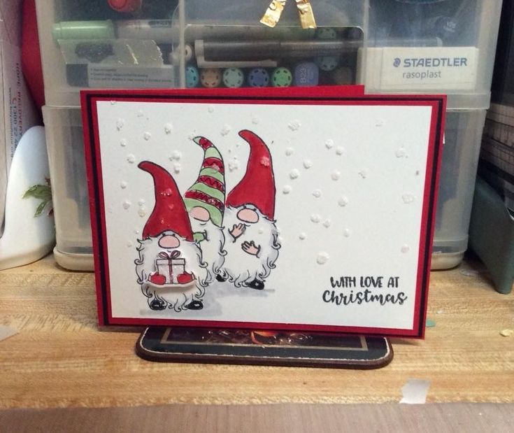 a christmas card with two gnomes on it in front of some crafting supplies