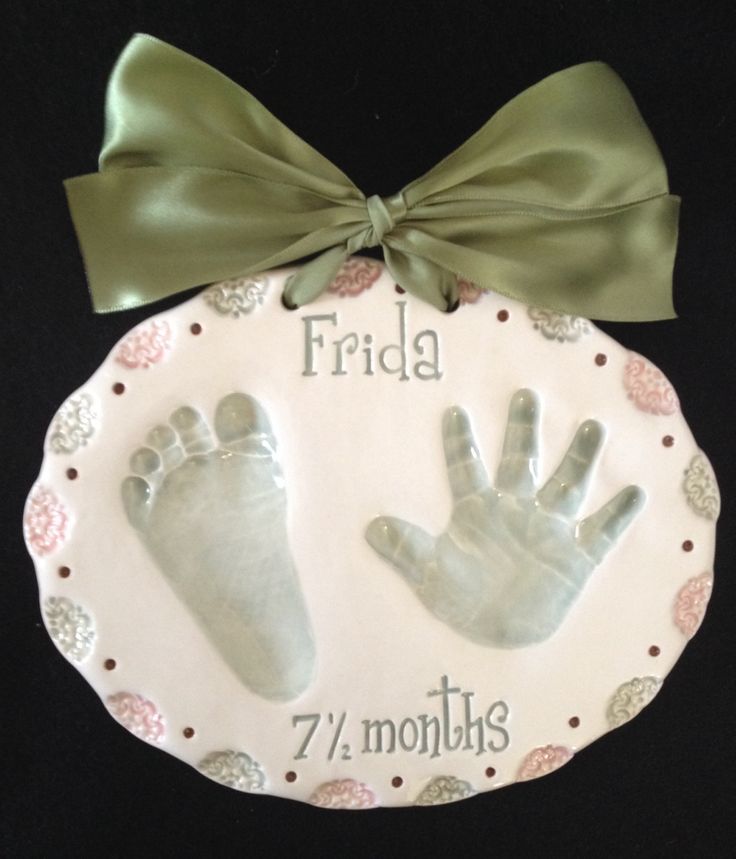 a baby's hand and foot print on a white plate with a green bow