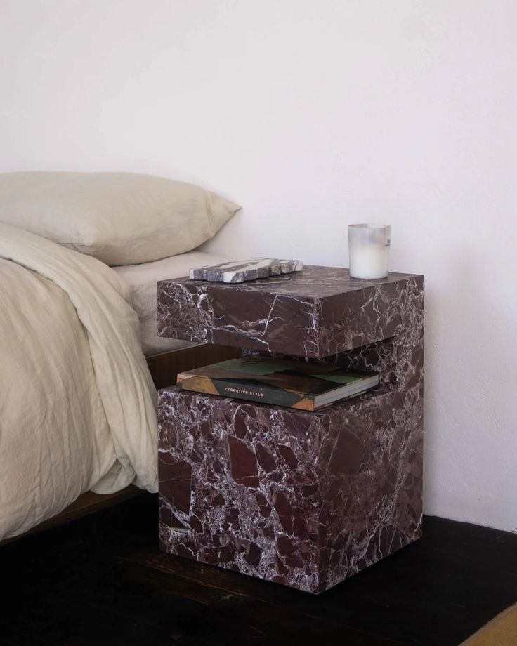 a marble side table with a book on it next to a white bed and pillows