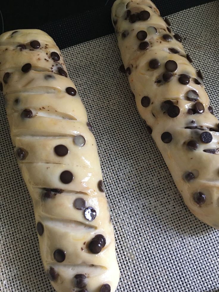 two doughnuts with chocolate chips on them sitting on a baking sheet, ready to be baked